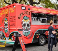 a woman standing in front of a red food truck with skulls painted on the side