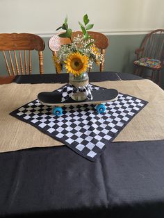 a vase with flowers and a skateboard on top of a black tableclothed placemat