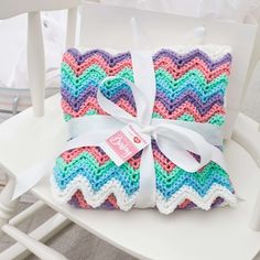 two colorful crocheted blankets tied together on a white chair with a white ribbon