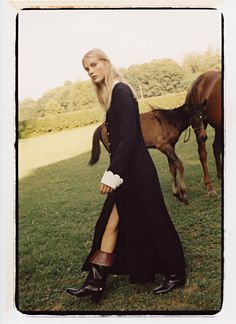 a woman in a long black dress walking next to a horse