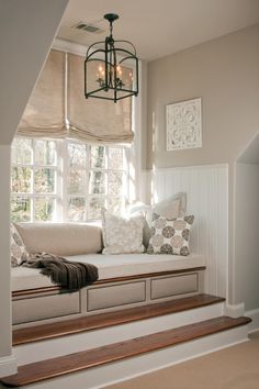 a window seat with some pillows on it and a light fixture hanging from the ceiling