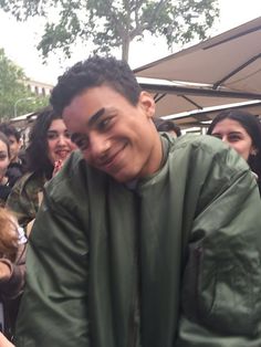 a man in a green jacket is smiling for the camera while people stand around him