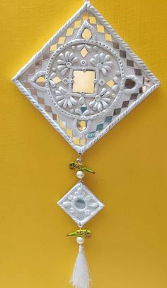 a decorative wall hanging on the side of a yellow wall with white decorations and tassels