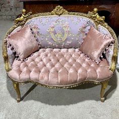 a pink and gold couch sitting on top of a floor next to a wooden table