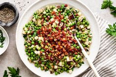 a white plate topped with peas and bacon next to two bowls filled with seasoning