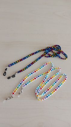 three lanyards with multicolored beads are on a white surface and one has a black metal hook