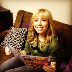 a woman sitting on top of a couch holding a pillow and reading a comic book