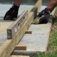 two men are working on some wooden pieces in the grass and one man is using a saw to cut wood