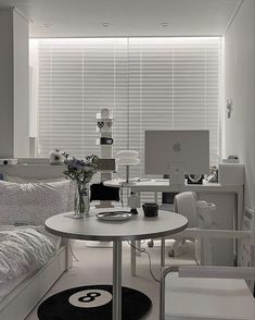 a white room with a bed, desk and computer on the table in front of it