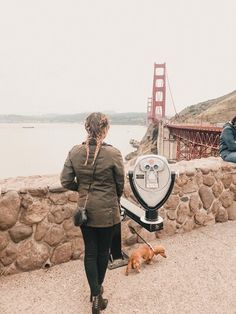 two people and a dog are looking at the golden gate bridge