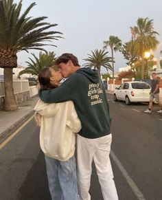 a man and woman kissing on the street with palm trees in the backgroud