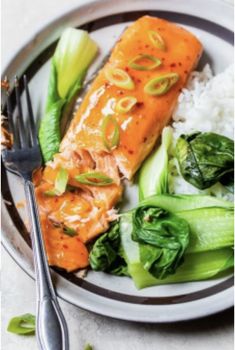 a plate with salmon, rice and greens on it next to a knife and fork