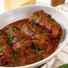 a white bowl filled with meat covered in sauce and garnished with parsley