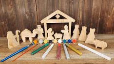 a wooden nativity scene with crib, spoons and paintbrushes in front of it