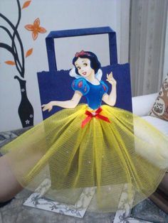 there is a doll sitting on the bed wearing a yellow dress and red bow around her neck