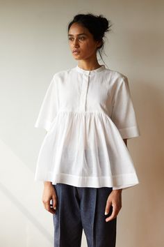 Playful top in pristine white khadi. Partial placket with a single button revealed at the neck. Gentle gathers at the yoke seam. Three quarter length sleeves. Khadi is a traditional, handwoven fabric native to India. The thread is first hand spun on a spinning wheel. The fabric is then woven on a handloom. The fabric for this garment has been woven by rural women determined to build a better life. Cotton Short Tops, Cotton Tops Designs, White Summer Tops, Streetwear Inspo, Handwoven Fabric, Stylish Dress Book, Shirts Design, Spinning Wheel, Cotton Top