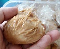 a person holding an unpeeled piece of food in their hand with plastic wrap around it