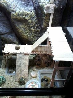 a toy house made out of wood sitting on top of sand in front of a rock