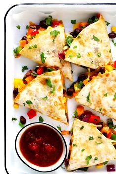 several quesadillas on a white platter with salsa and condiments