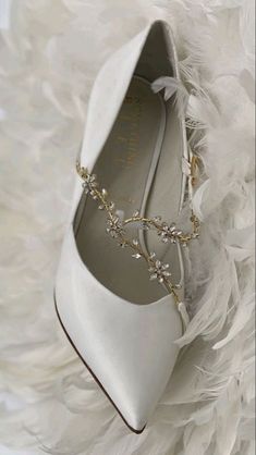 a pair of white shoes with feathers on the floor and one shoe has a gold chain attached to it