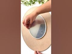 a person is holding a round mirror with their hands on the edge and another hand reaching for it