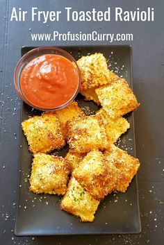 air fryer toasted ravioli on a black plate with dipping sauce in the middle