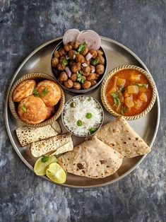 a metal plate topped with different types of food on top of a table next to rice and pita bread