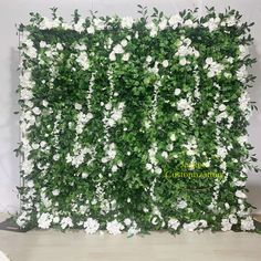 white flowers are growing on the side of a green wall with greenery behind it