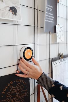 a woman's hand is pressing the button on a wall mounted clock that reads 70