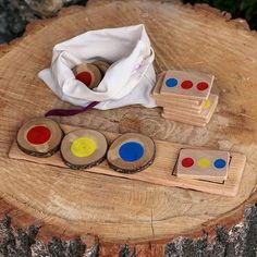 four wooden pegs with different colored dots on them sitting on a tree stump next to a white bag