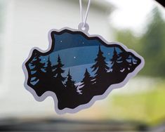 an ornament hanging from the side of a car window with trees on it