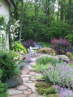 a stone path leads to a garden with purple flowers and greenery in the background