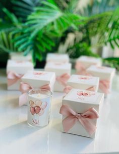 small white boxes with pink bows are sitting on a table next to a candle holder