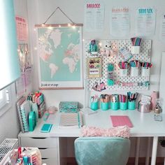 a white desk topped with lots of office supplies next to a wall covered in posters