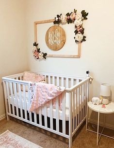 a white crib with pink and white flowers on the wall next to a table