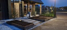 the front entrance of a building at night with lights on and plants in raised beds