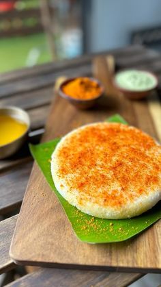 some food is sitting on a green plate with sauces in bowls behind it and a wooden table