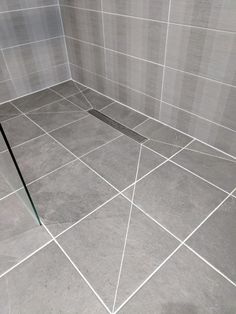 a tiled bathroom with a glass shower door and tile flooring on the walls, in grey tones