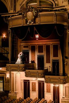 the bride and groom are standing on the balcony of an old theater stage with their arms around each other