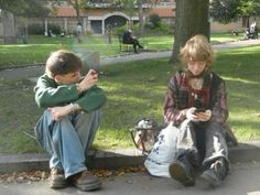 two young boys sitting on the ground next to each other looking at their cell phones