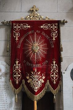 a large red and gold cloth hanging from the side of a church wall next to a plaque