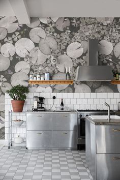 a kitchen with white tile flooring and stainless steel appliances in front of a floral wallpaper