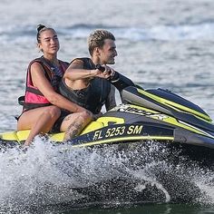 a man and woman riding on the back of a yellow and black jet ski in the ocean