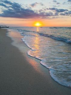 the sun is setting over the water at the beach with waves coming in to shore