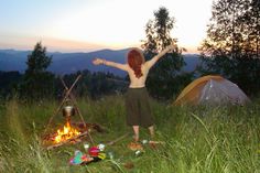 a woman standing in front of a campfire with her arms outstretched