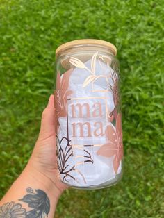 a person holding up a mason jar with the words mama on it in front of some grass