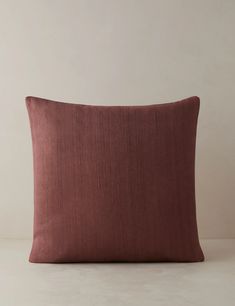 a pink pillow on a white surface with a light brown wall in the back ground