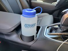 a blue and white water bottle sitting on the center console of a car, next to a charger