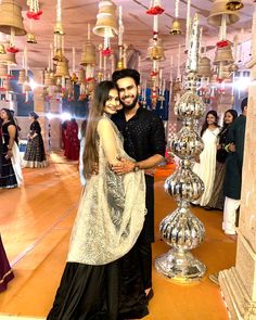 a man and woman pose for a photo in front of many hanging bells on the ceiling