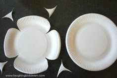 two white paper plates sitting next to each other on a black counter top with cut out pieces of paper